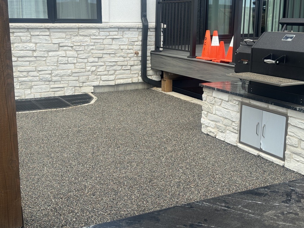 Supplied installation photograph of resin-bound stone surfacing beside masonry and an outdoor kitchen